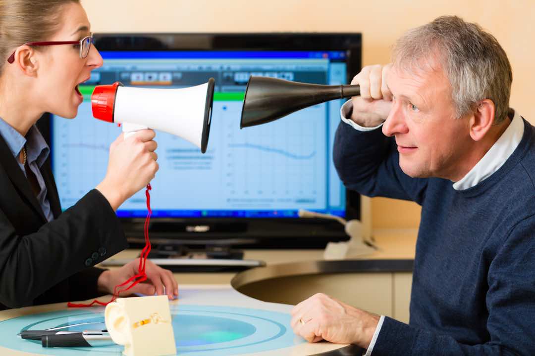 Woman talking into megaphone to a man holding a ear horn to his ear